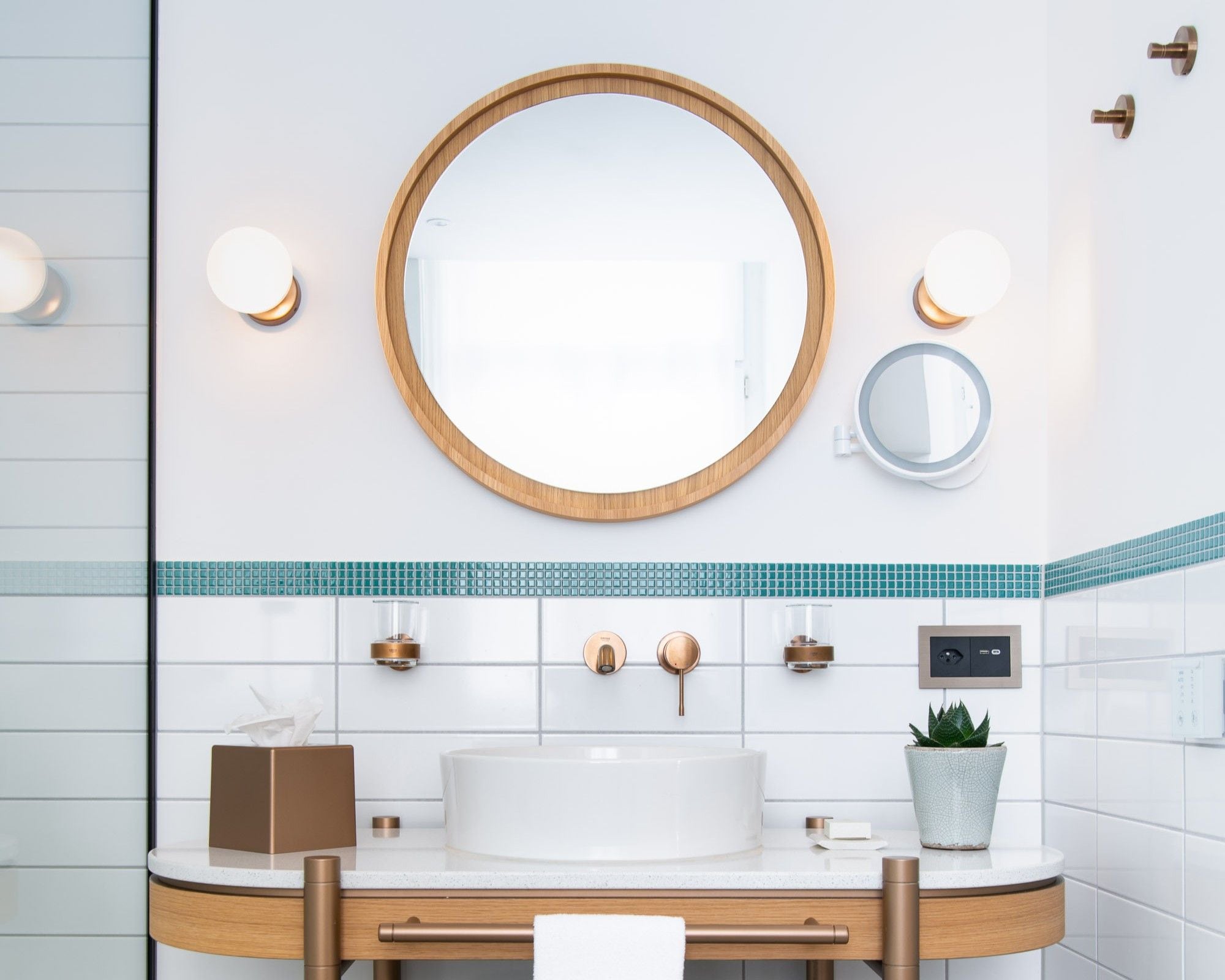 Un baño moderno con un espejo redondo grande, un lavabo blanco y una planta en maceta.