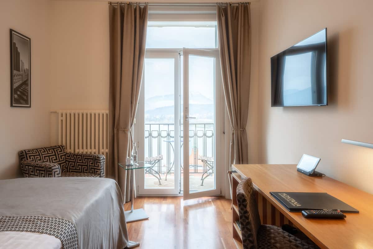 Een hotelkamer met een bed, een bureau met een laptop, een televisie en uitzicht op bergen.
