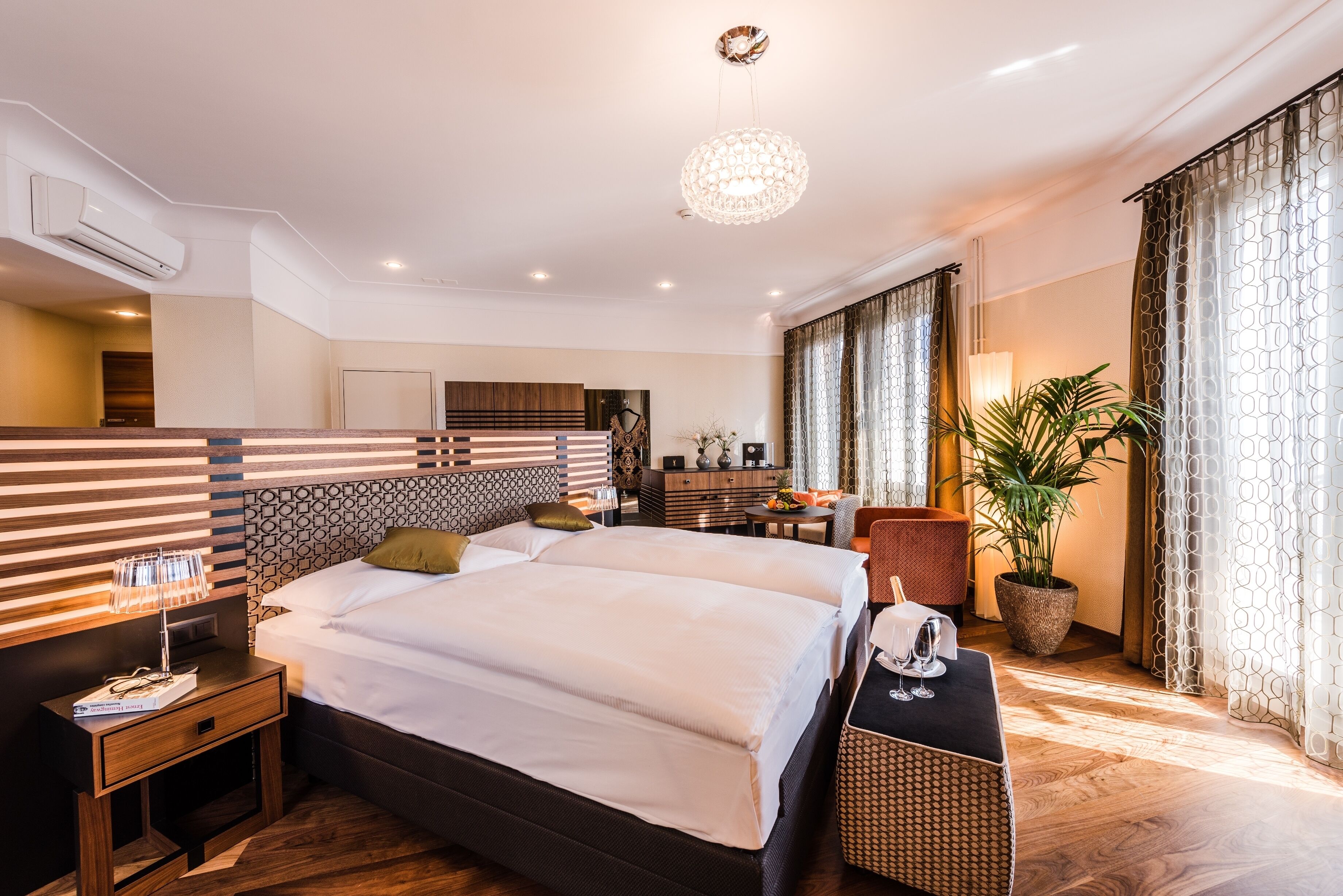 Une chambre d’hôtel moderne avec un grand lit, des tables de chevet, un bureau et une plante en pot.