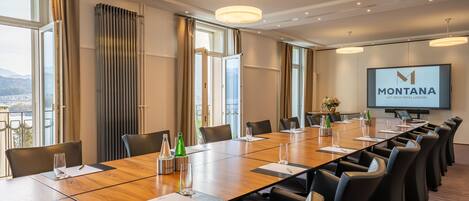 A conference room with a long table, chairs, a projector screen, and a view of the mountains.