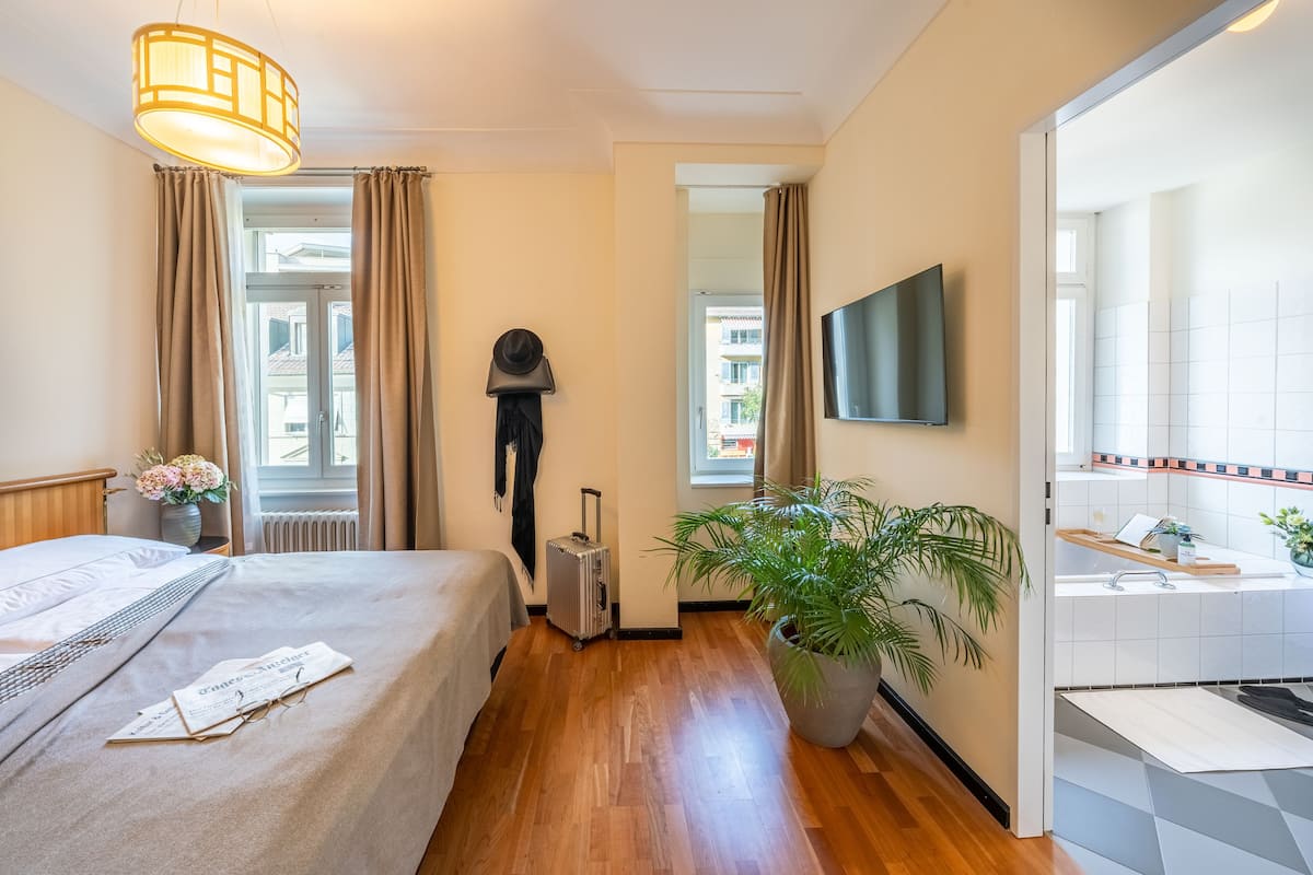 Hotelkamer met een bed, een koffer, een potplant, een televisie en een badkamer die door een open deur zichtbaar is.