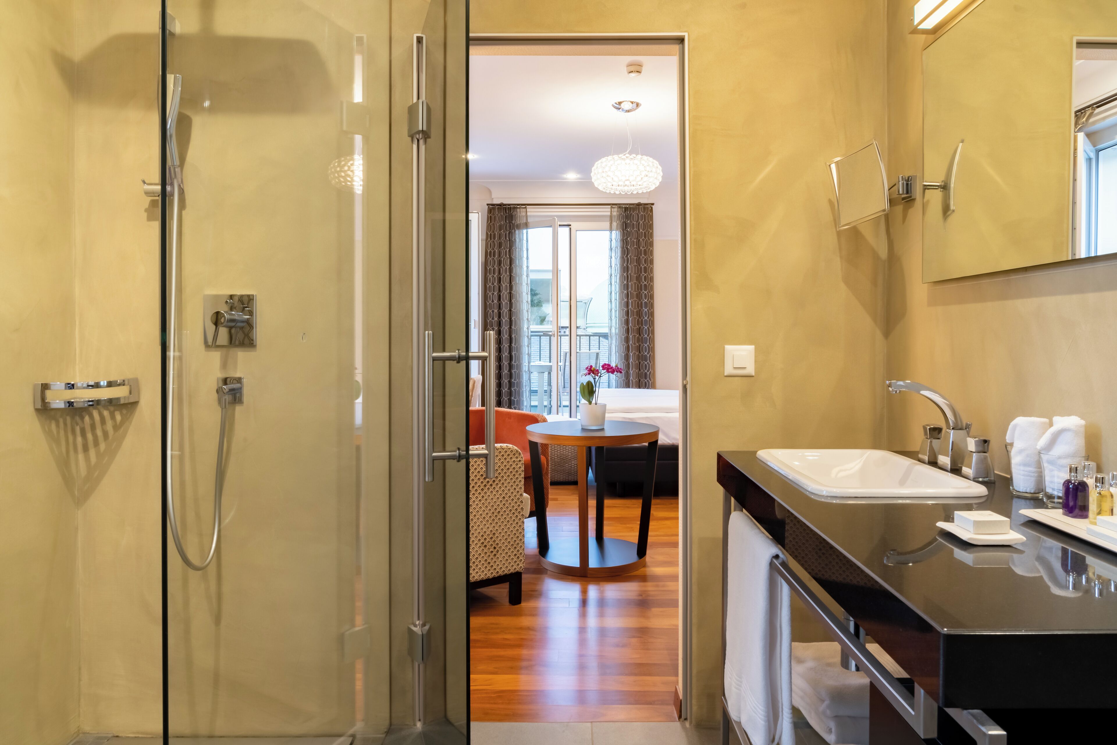 A modern bathroom with a glass-enclosed shower, a large mirror, and a vanity with a sink and toiletries.