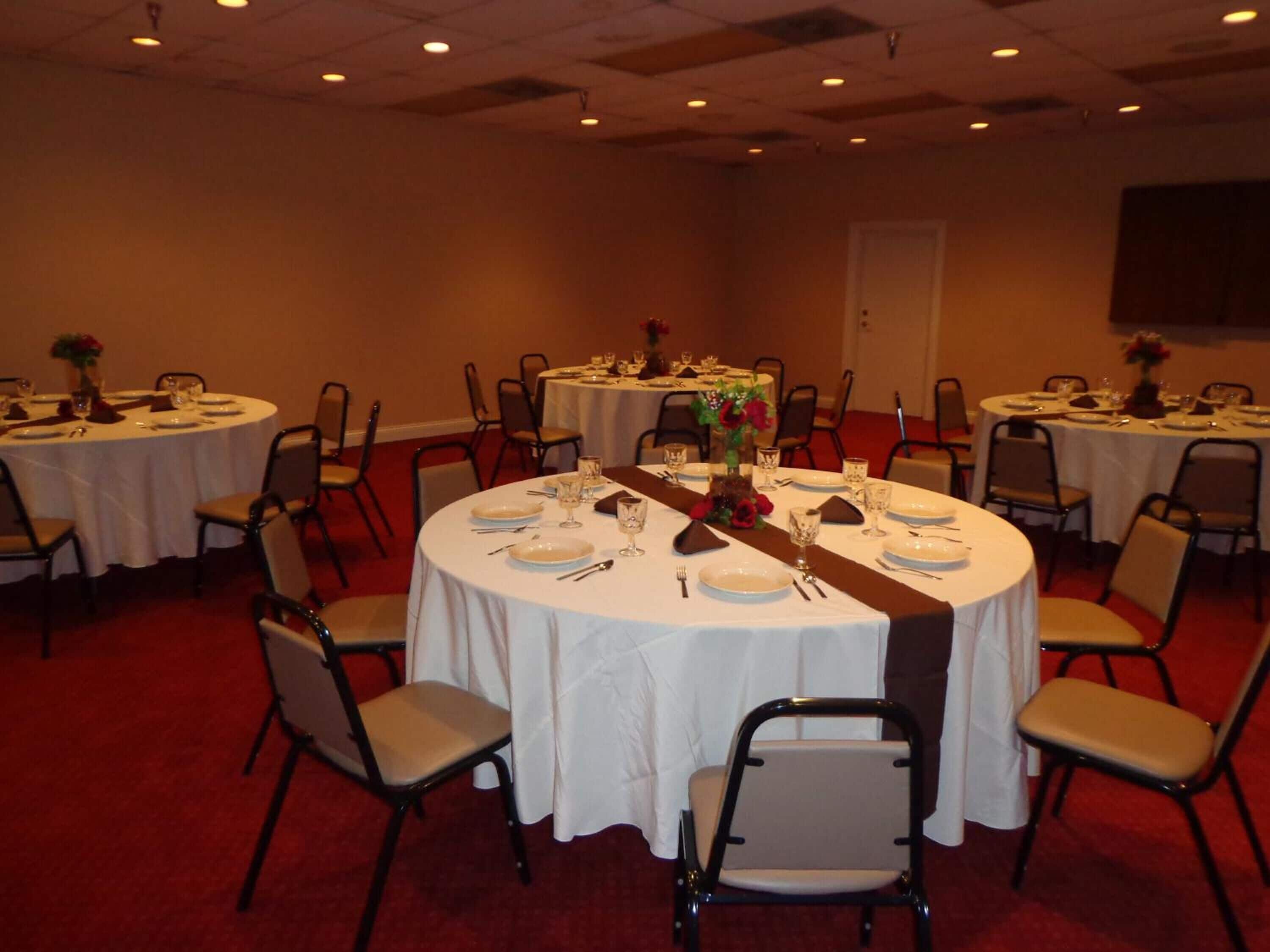 A conference room with multiple round tables, each set with plates, cutlery, and glasses.