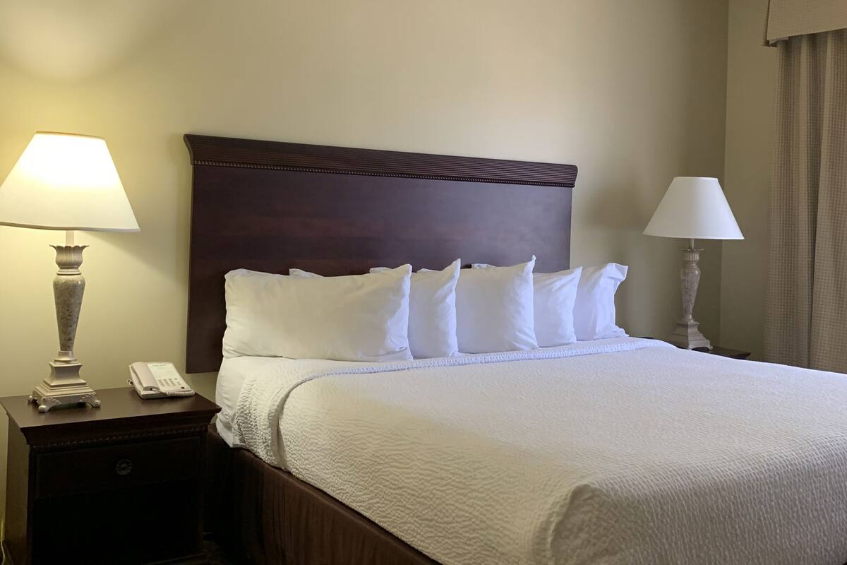 A hotel room with a large bed, two bedside tables, a telephone, and a lamp on each side.