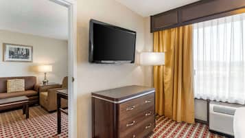 Habitación de hotel con una televisión de pantalla plana montada en la pared, un escritorio con lámpara, un sofá, un aparador y una ventana con cortinas.