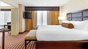 Een hotelkamer met een groot bed, een bureau, een stoel, een televisie en een raam met gordijnen.