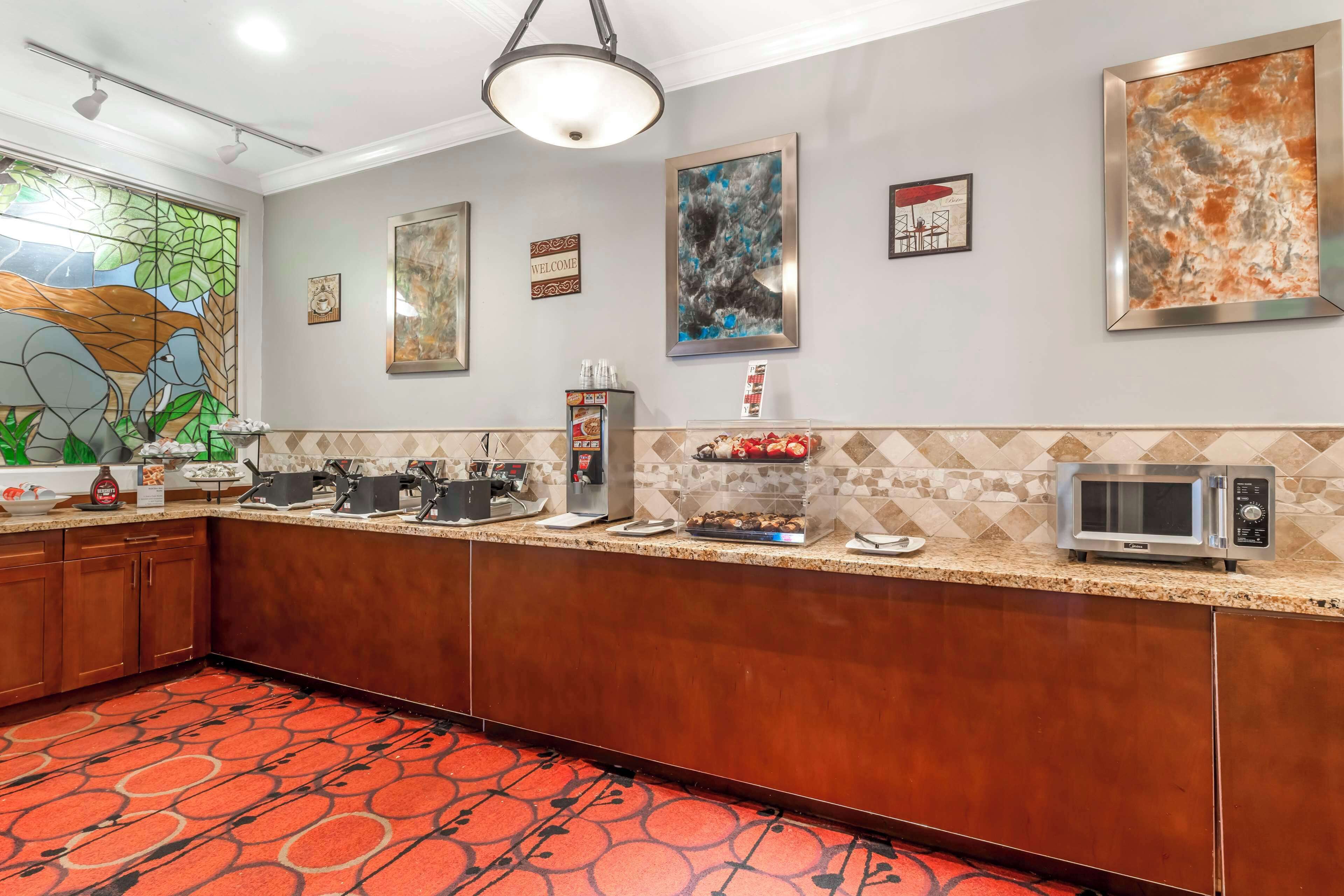 A hotel kitchen with a long counter, microwave, coffee machine, and various food items.