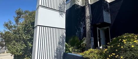 Une enseigne d’hôtel portant le symbole d’accessibilité pour les personnes en fauteuil roulant, entourée d’un jardin aménagé avec différentes fleurs et d’un palmier.