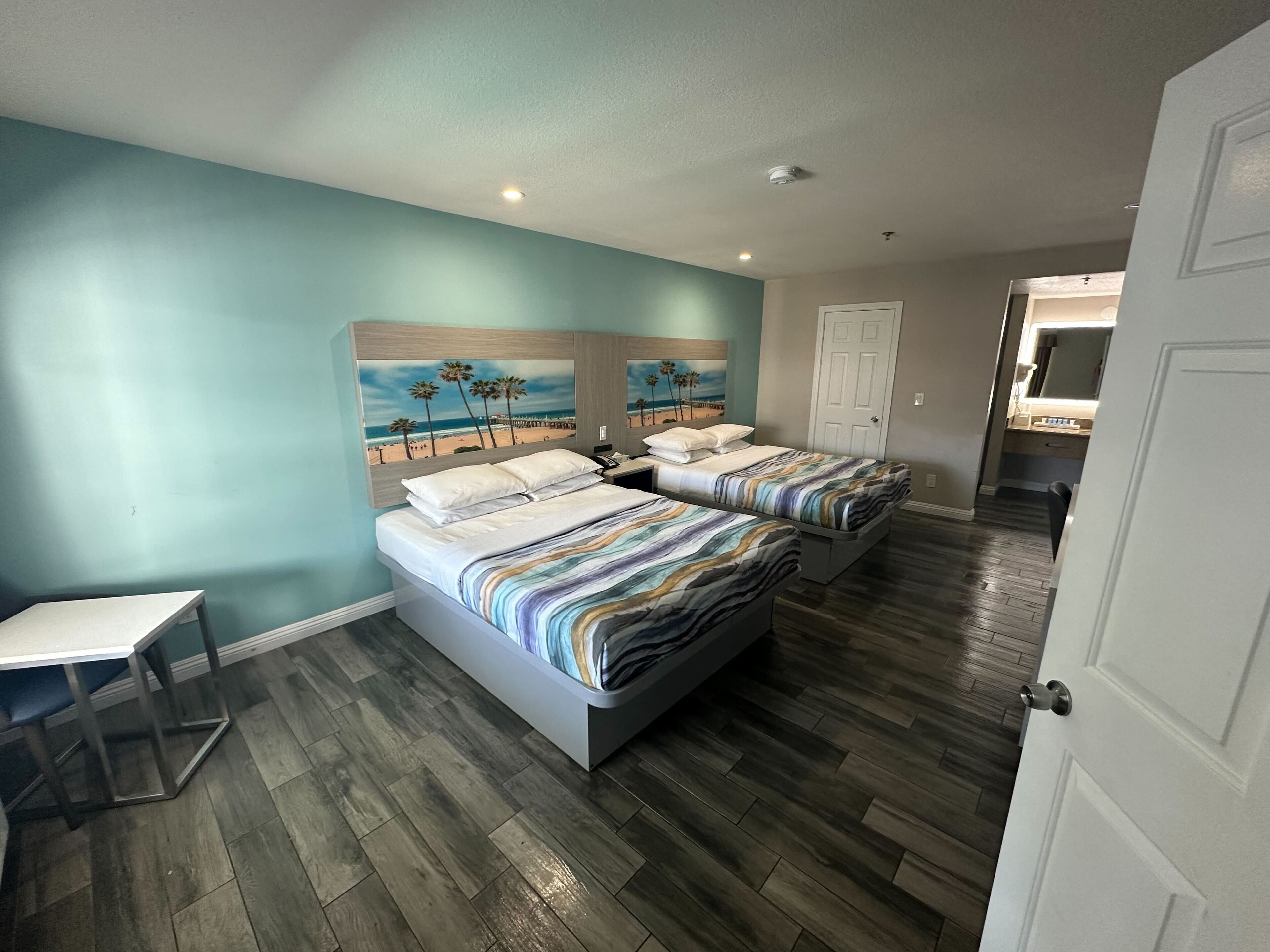A hotel room with two beds, a desk, and a painting of a beach scene on the wall.