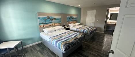 A hotel room with two beds, a desk, and a painting of a beach scene on the wall.