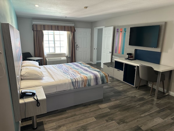 A modern hotel room with a bed, desk, chair, TV, and wardrobe.
