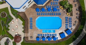 An aerial view of a hotel with a central swimming pool surrounded by sun loungers and umbrellas, a garden area with a circular flower bed, and a building with a blue roof. - Hilton Chicago/Oak Brook Hills Resort & Conference Center (Oak Brook)