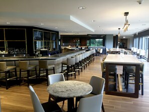 A modern bar area with a long counter, bar stools, and a seating area with round tables and chairs. - Hilton Chicago/Oak Brook Hills Resort & Conference Center (Oak Brook)
