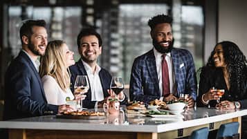 Un grupo de personas sentadas en una mesa con comida y bebidas, en un ambiente interior moderno con grandes ventanales.