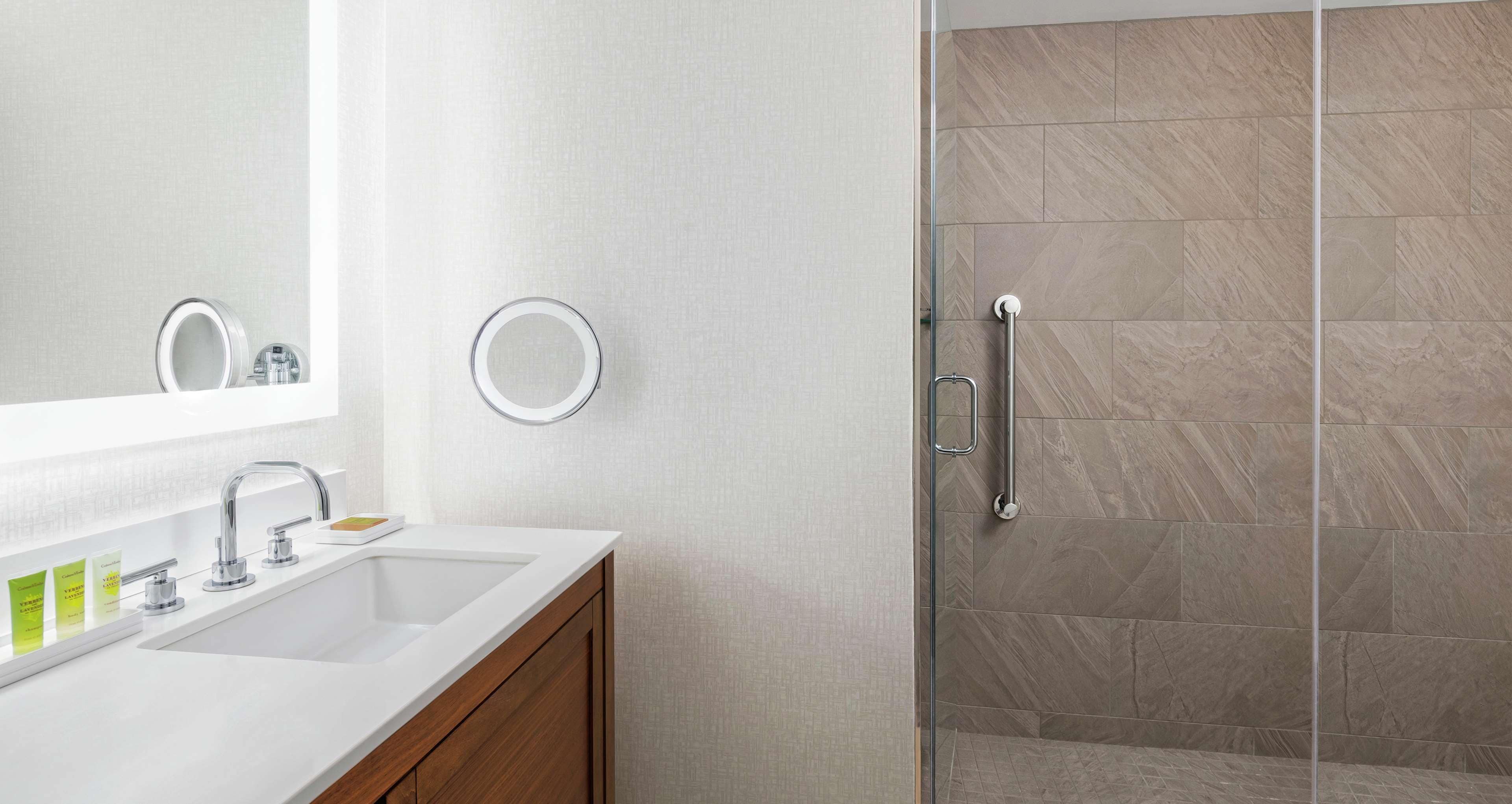 Ein modernes Badezimmer mit einem weißen Waschbecken, einem Spiegel und einer Duschkabine aus Glas.