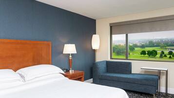 A hotel room with a bed, a desk, a chair, and a window with a view of a golf course.