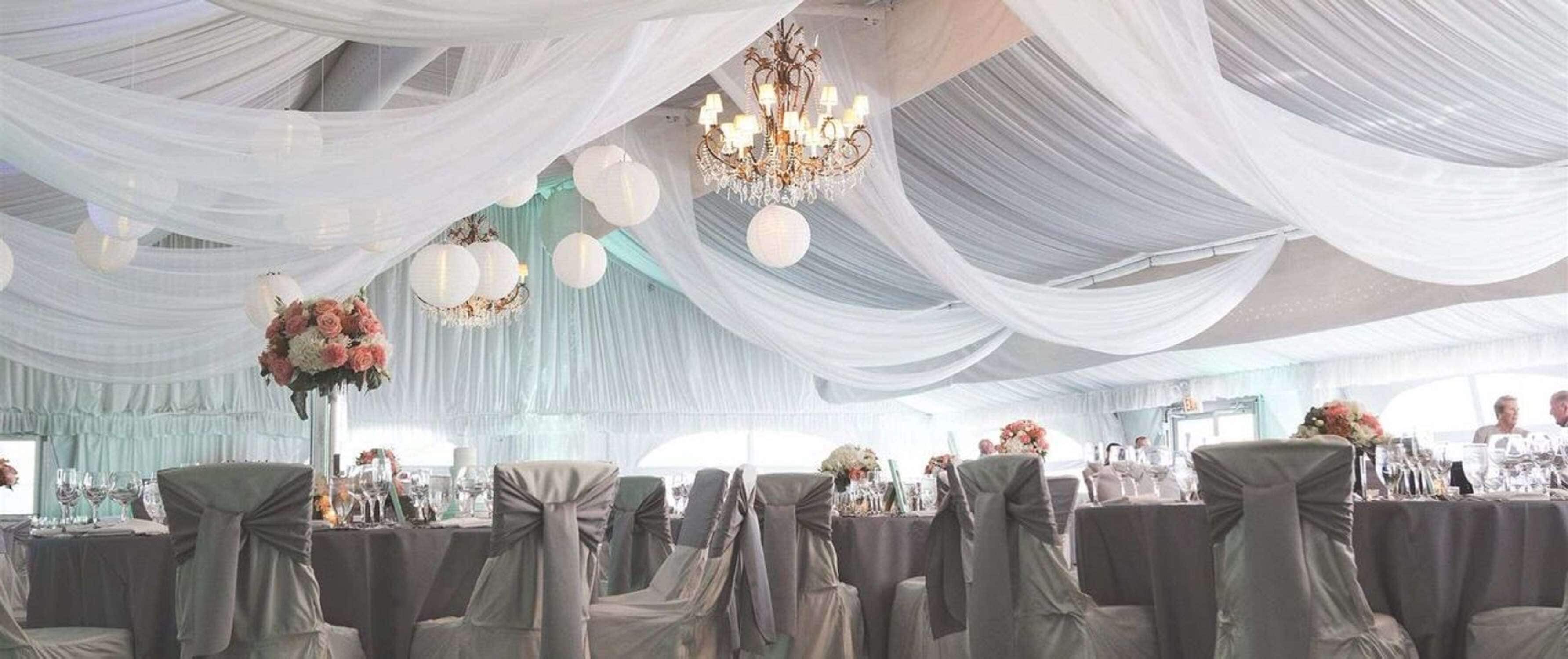 A banquet hall with tables covered in tablecloths, chairs with sashes, and a chandelier.