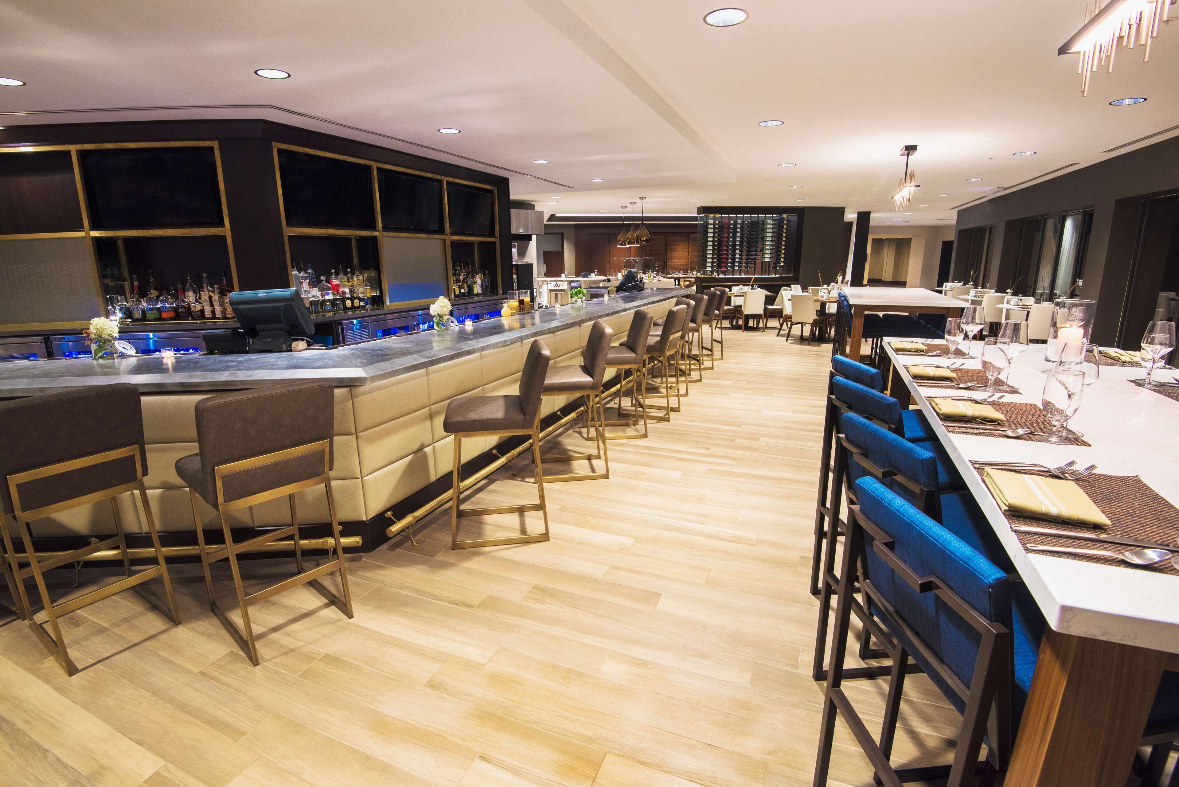 Un moderno bar con una barra larga, taburetes y una zona de estar con mesas y sillas.