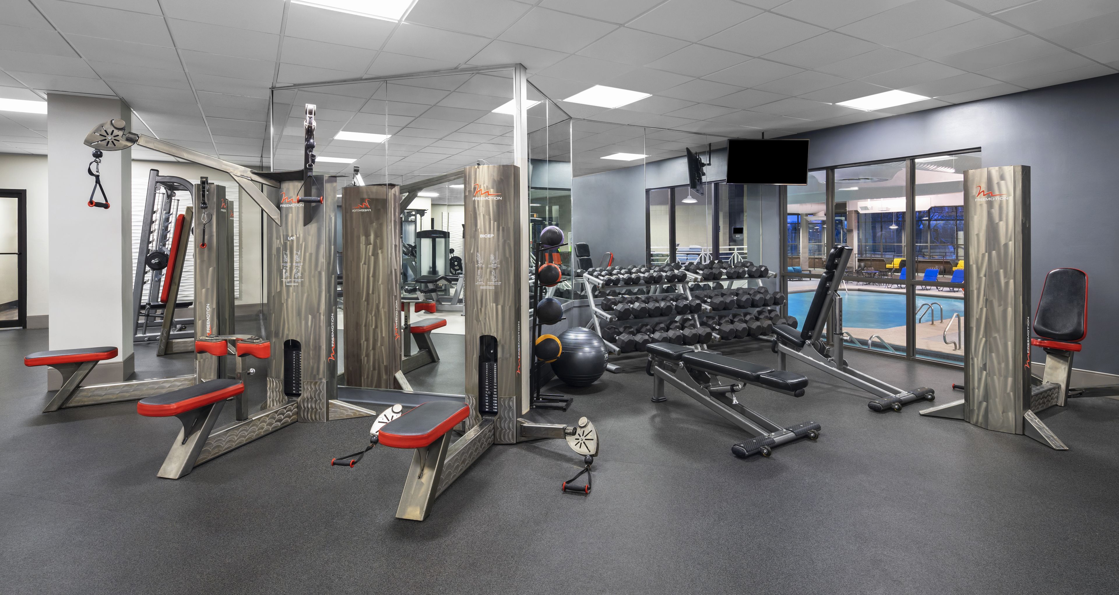 A gym with various exercise equipment, a pool, and a mirrored wall.