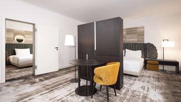Une chambre d’hôtel avec un lit, une table ronde, une chaise jaune, une armoire de couleur sombre et une lampe.