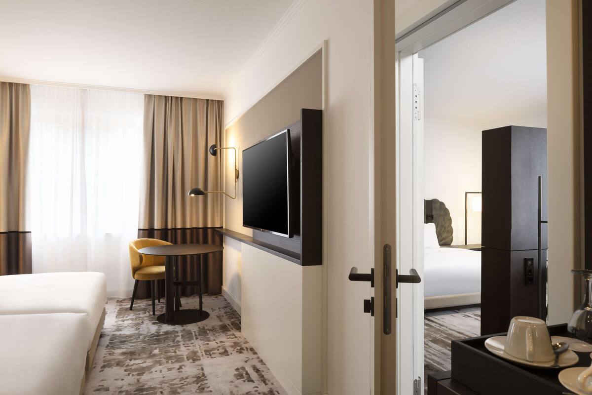 A hotel room with a bed, a desk, a chair, a television, and a bathroom visible through an open door.