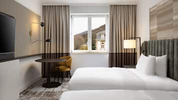 Ein Hotelzimmer mit Bett, Schreibtisch, Stuhl, Fernseher und einem Fenster mit Vorhängen.