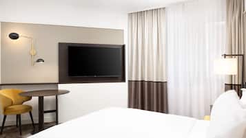 Une chambre d’hôtel avec un grand lit, un téléviseur à écran plat fixé au mur, une petite table ronde avec une chaise jaune et une lampe sur la table de chevet.