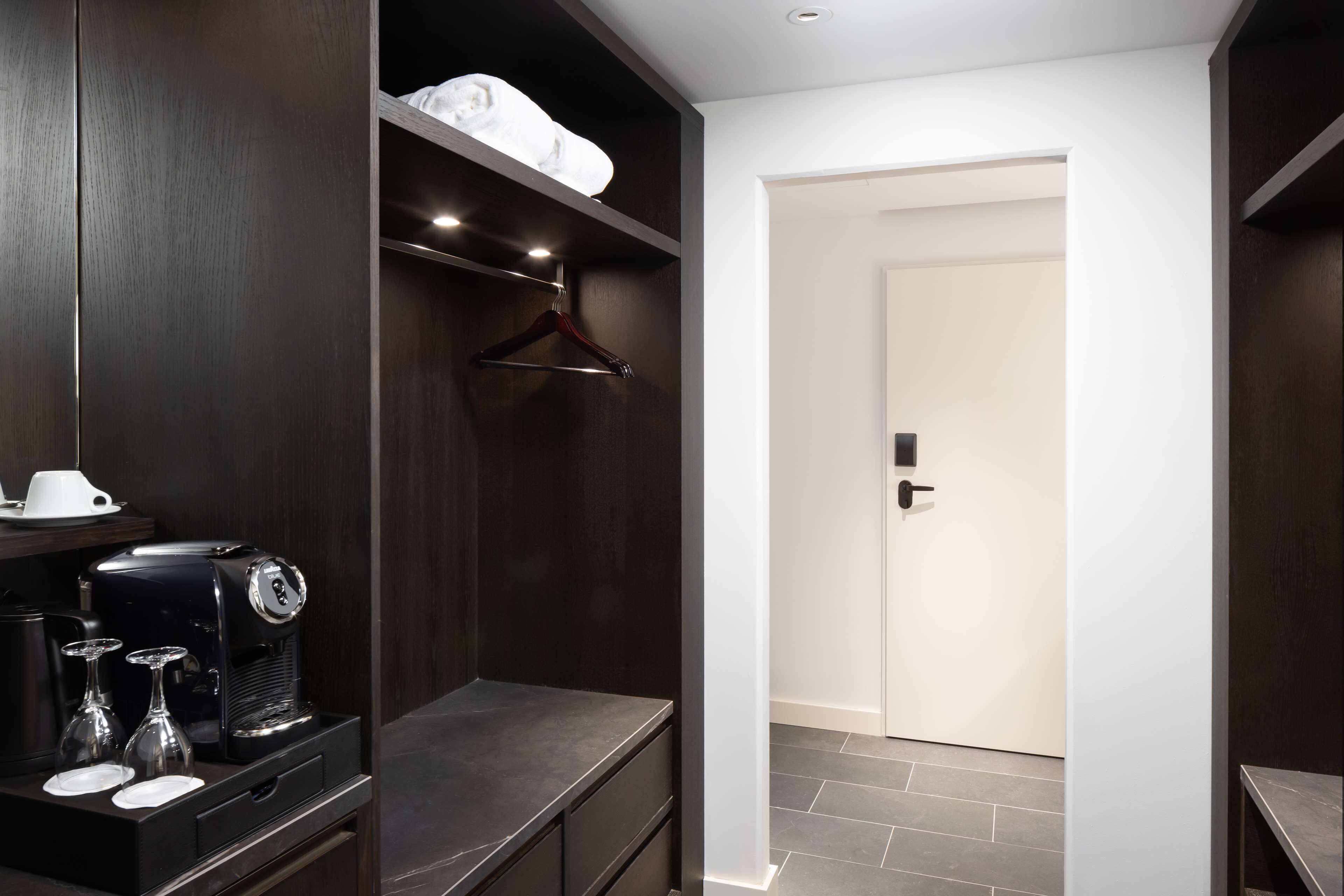 A modern hotel room with a dark wood wardrobe, a coffee machine, and a white door.