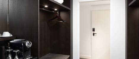 A modern hotel room with a dark wood wardrobe, a coffee machine, and a white door.