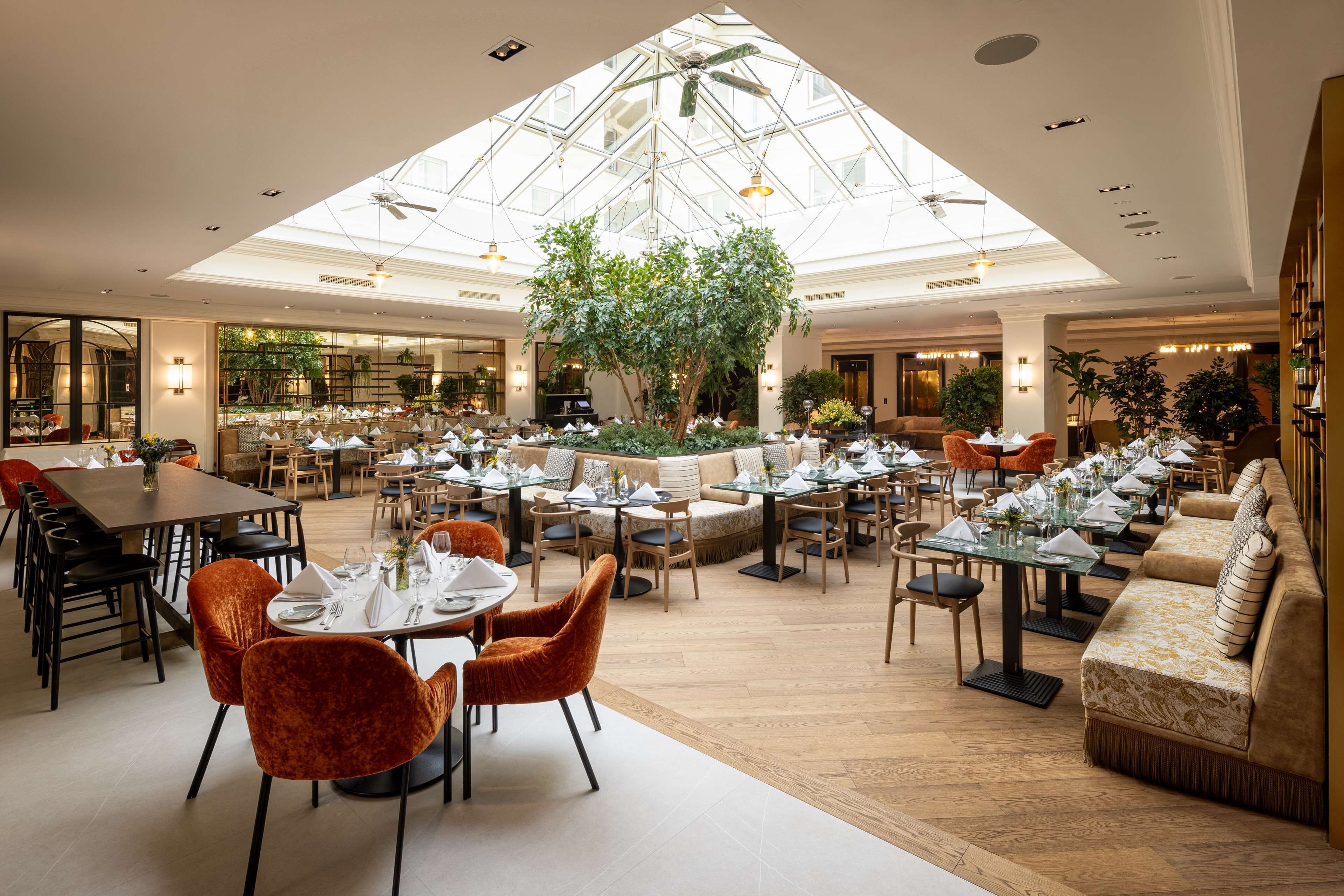 A spacious dining area with multiple tables and chairs, a central indoor garden, and a high ceiling with skylights.