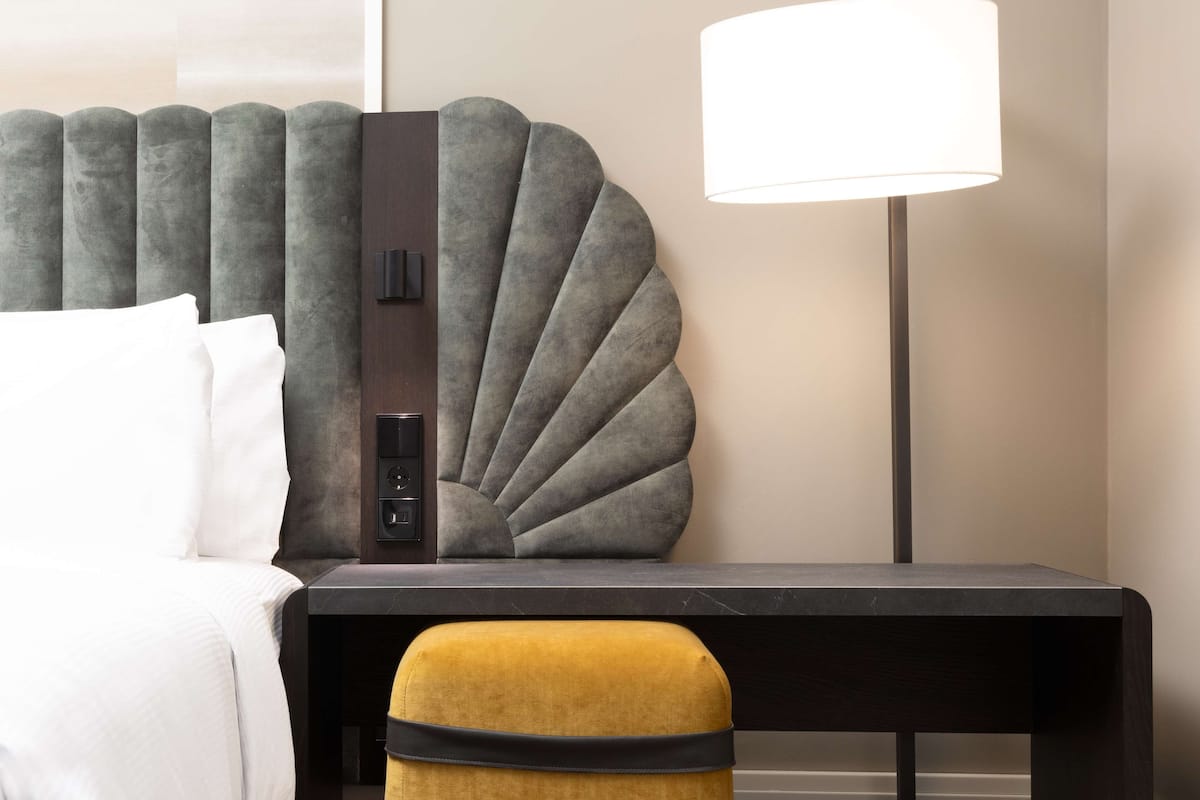 A hotel room with a bed, a nightstand, a lamp, and a decorative headboard.