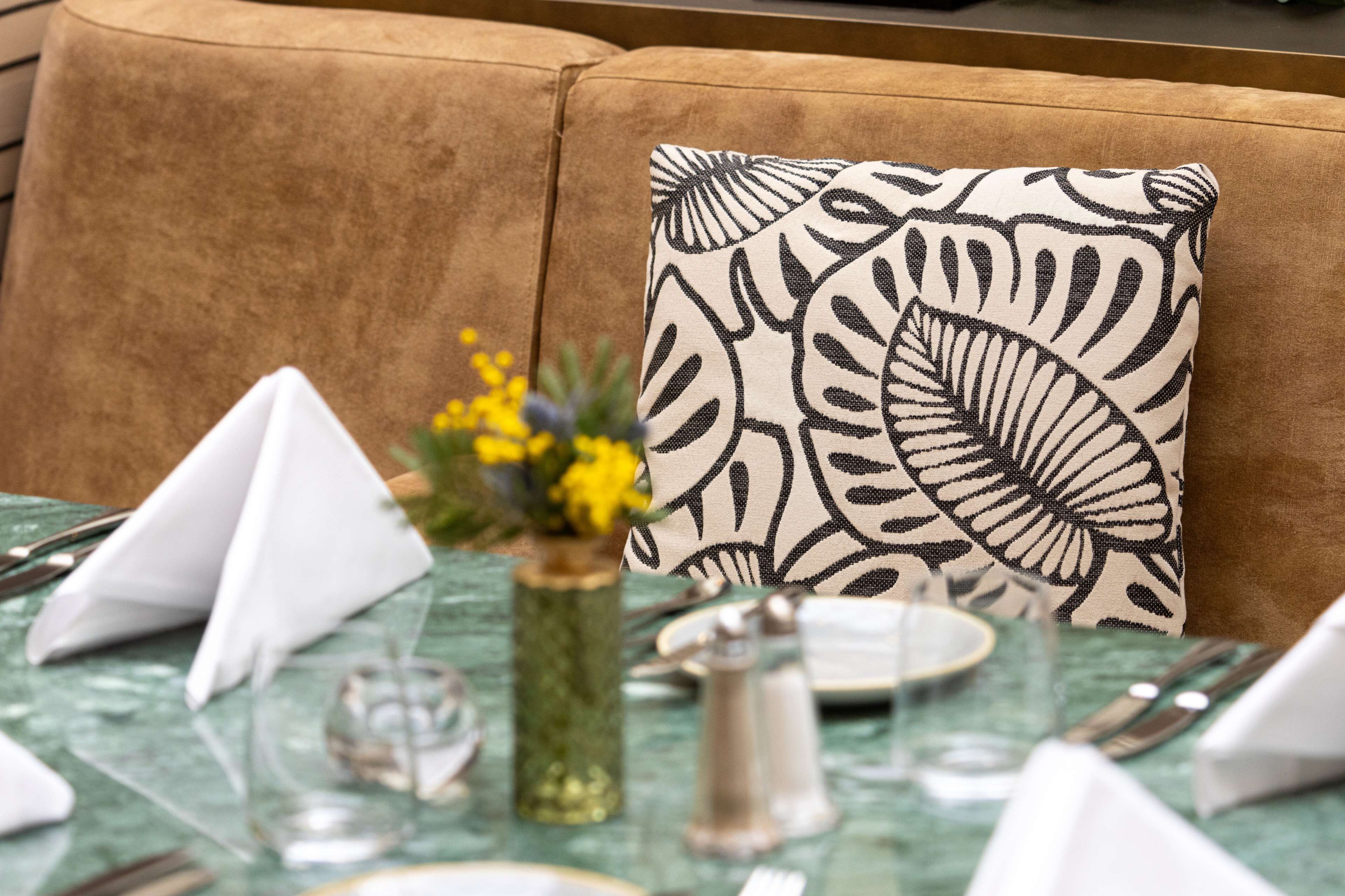 A dining table set with white napkins, a clear glass, a salt shaker, and a vase with yellow flowers.