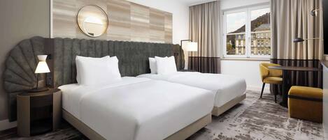 Une chambre d’hôtel avec deux lits, un bureau, une chaise et une grande fenêtre donnant sur un immeuble.