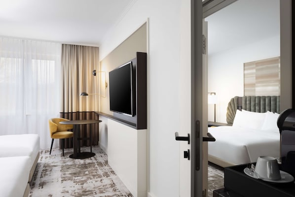 A hotel room with a bed, a TV, a desk with a chair, and a coffee table. - Hilton Heidelberg (Heidelberg)