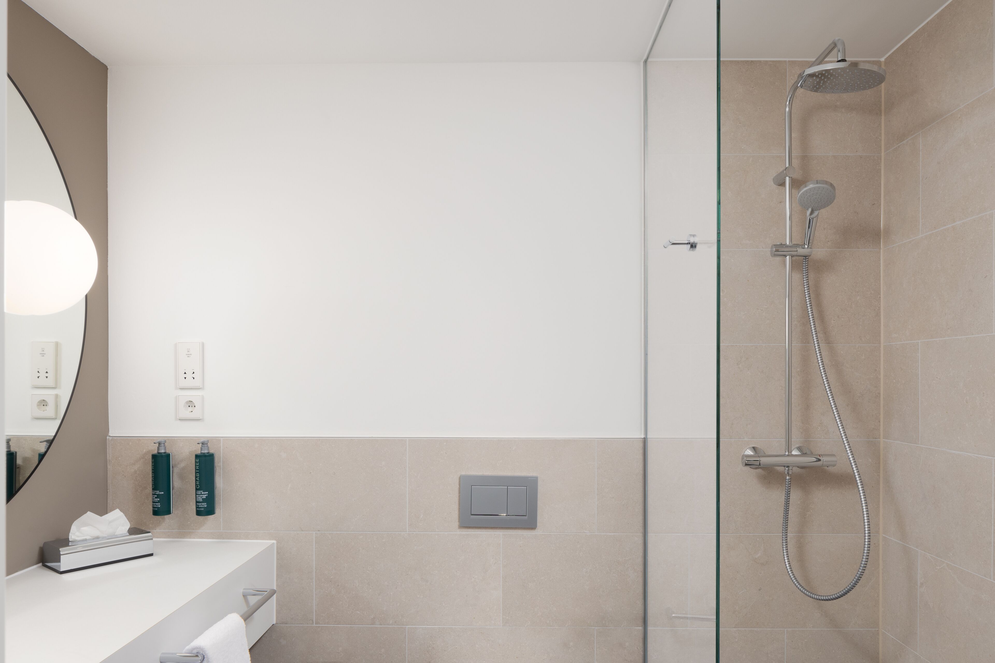 A modern bathroom with a glass-enclosed shower, a white vanity with a mirror, and two green bottles on the wall.