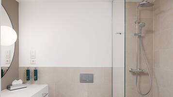 A modern bathroom with a glass-enclosed shower, a white vanity with a mirror, and two green bottles on the wall.
