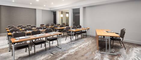 A conference room with multiple tables and chairs, carpeted flooring, and recessed lighting.