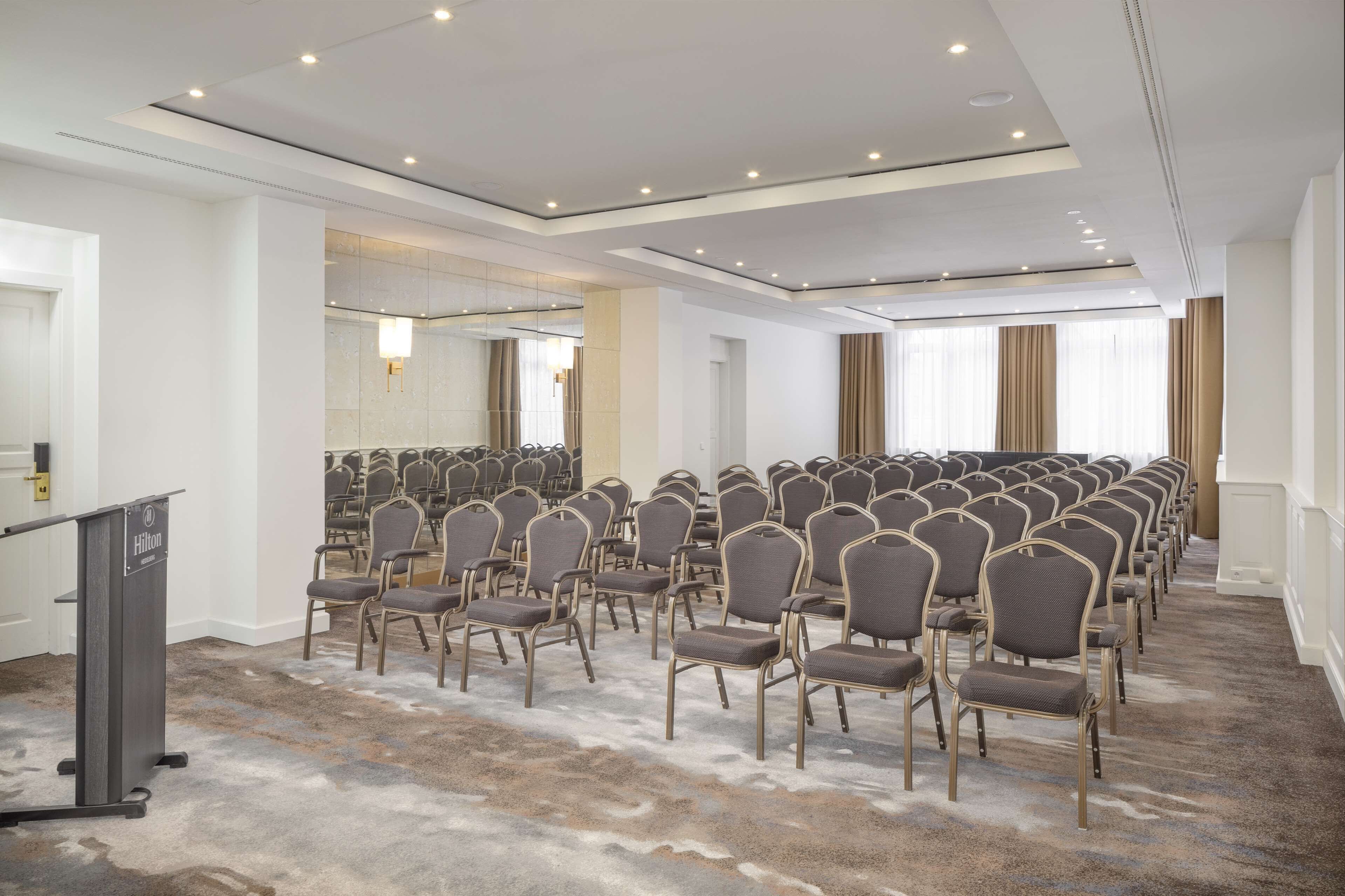 A conference room with rows of chairs, a podium, and a carpeted floor.