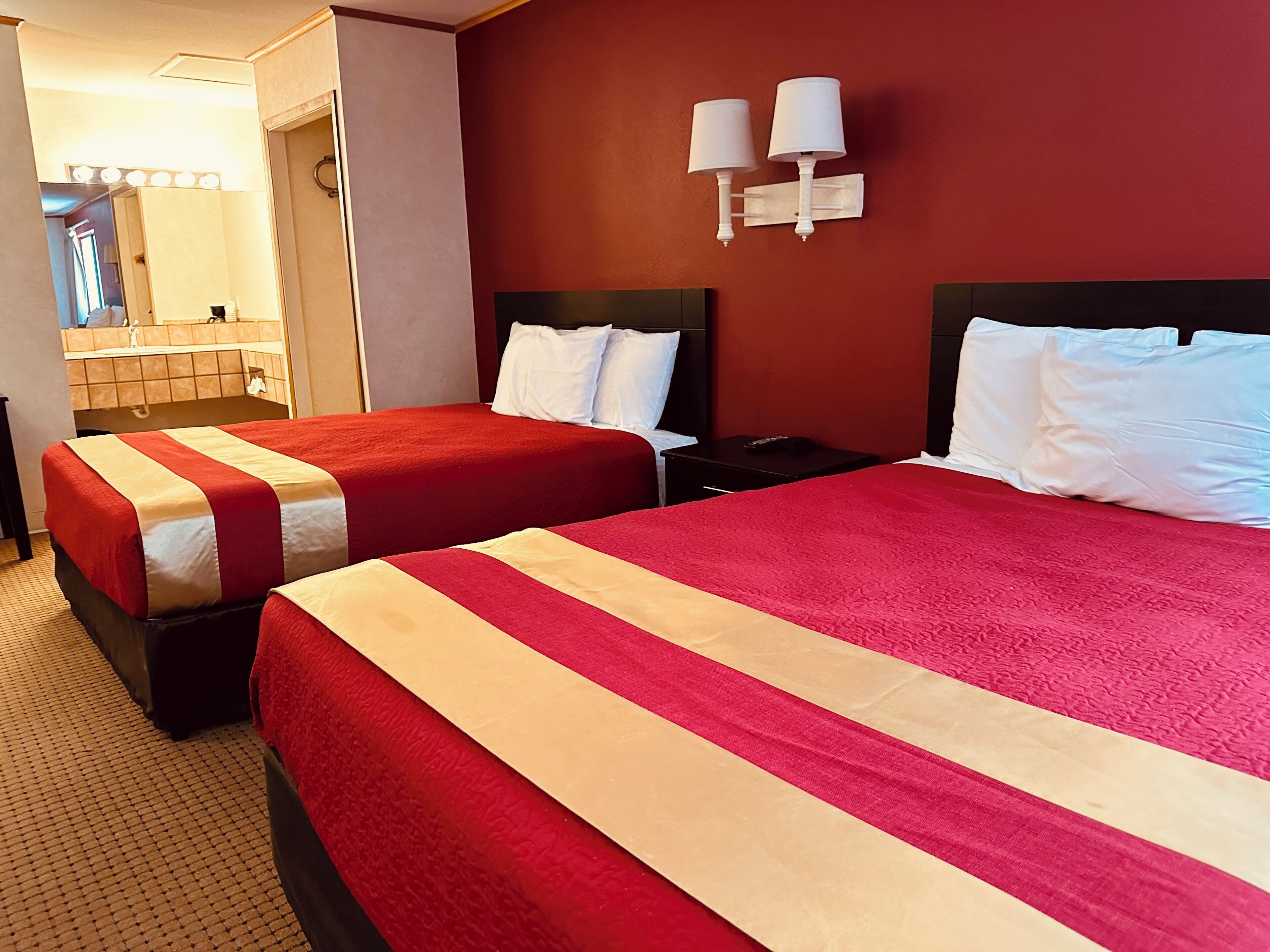 Une chambre d’hôtel avec deux lits, un miroir, une table de chevet et un mur rouge.