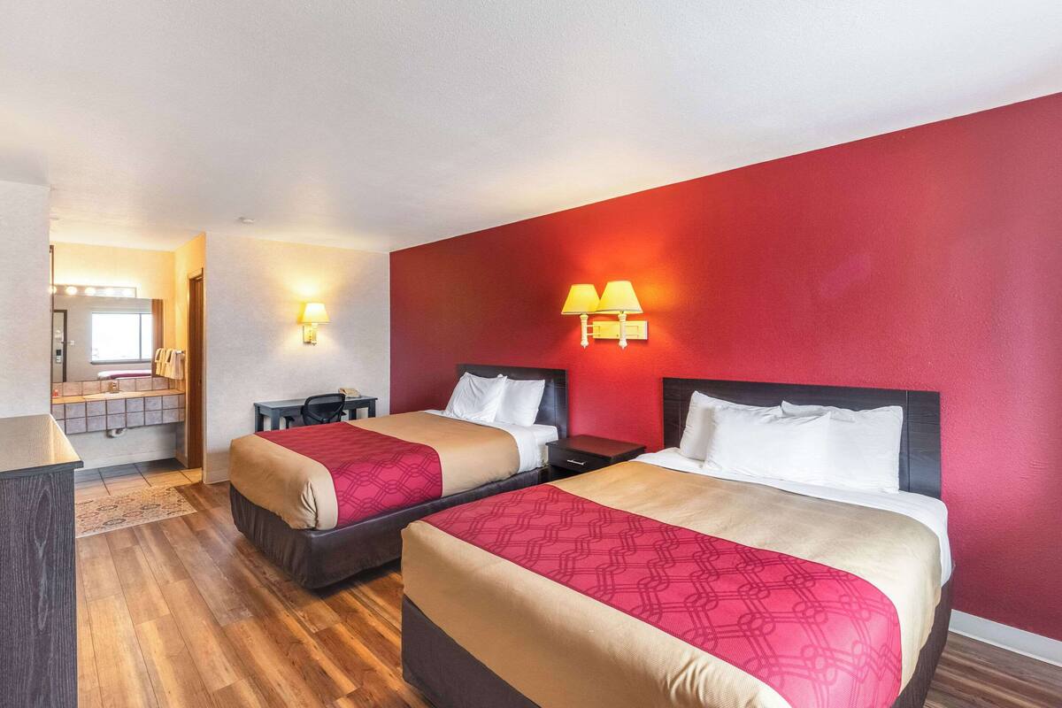A hotel room with two beds, a desk, and a mirror.