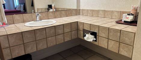 A modern bathroom with a sink, mirror, and towel dispenser.