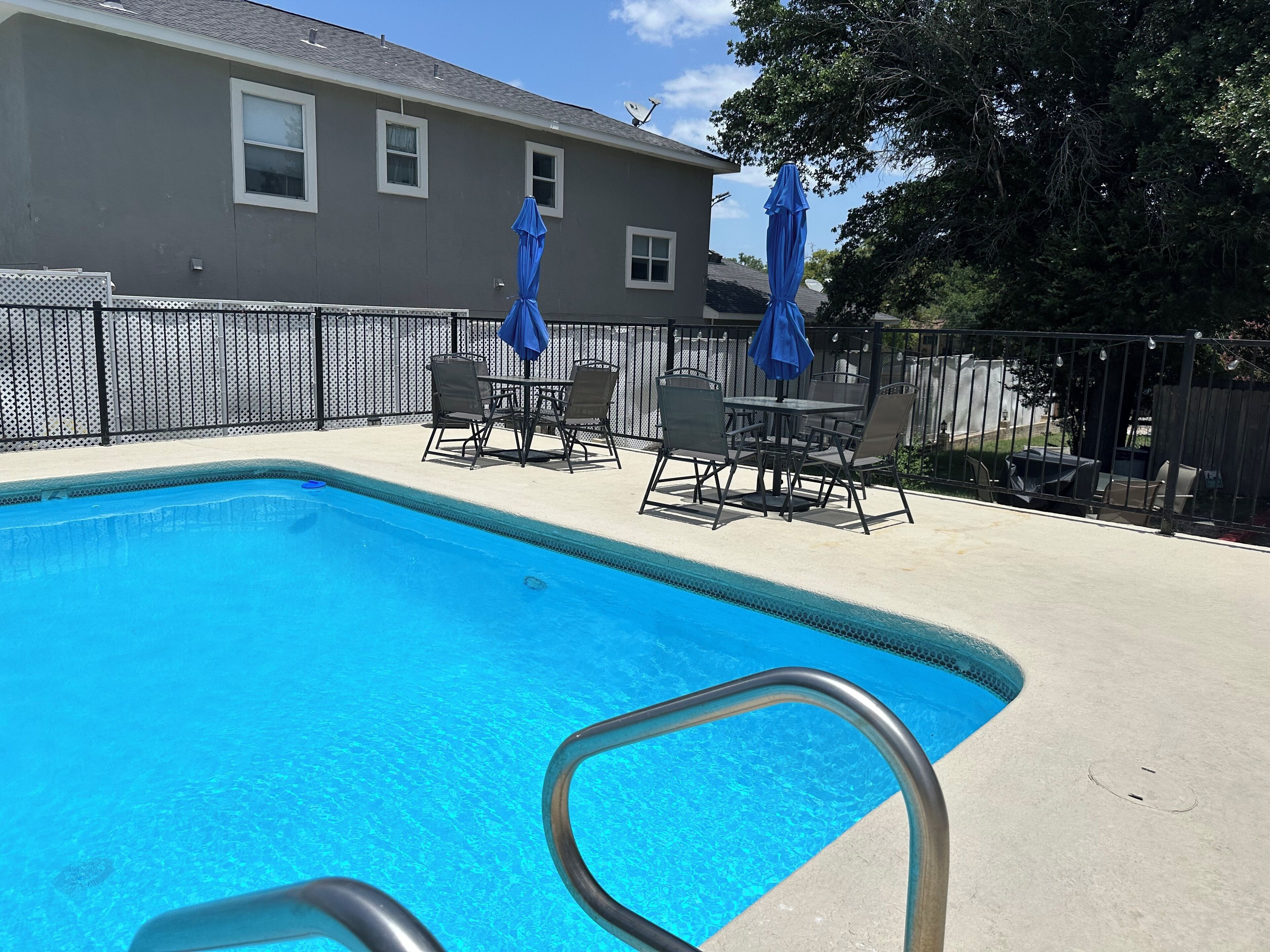 A swimming pool with a metal ladder, surrounded by a concrete deck and a metal fence.