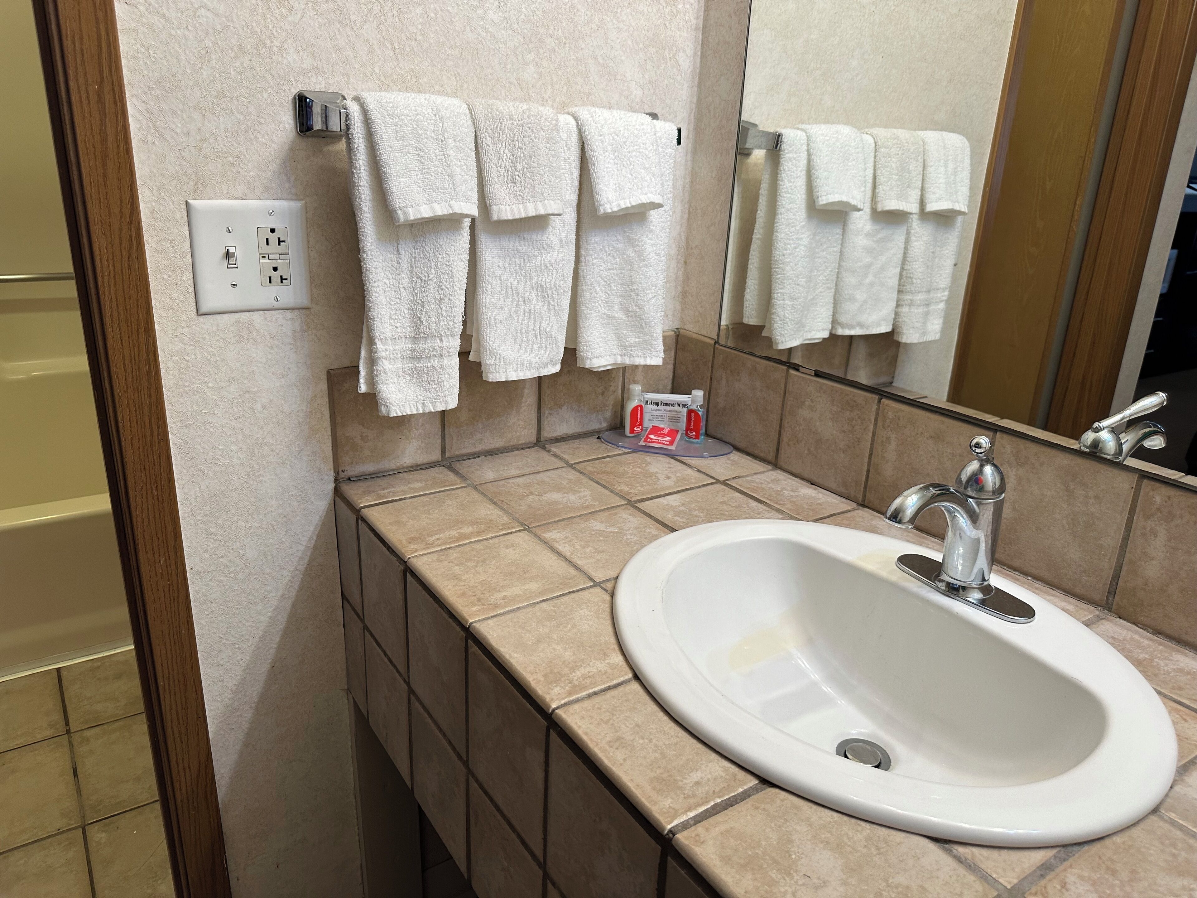 A bathroom with a white sink, a mirror, and multiple white towels hanging on a rack.