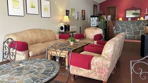 Un salon avec un canapé beige, un fauteuil à motifs floraux et une table ronde dont le plateau est orné de mosaïques. Les murs sont décorés de tableaux encadrés et une cheminée en pierre est présente.