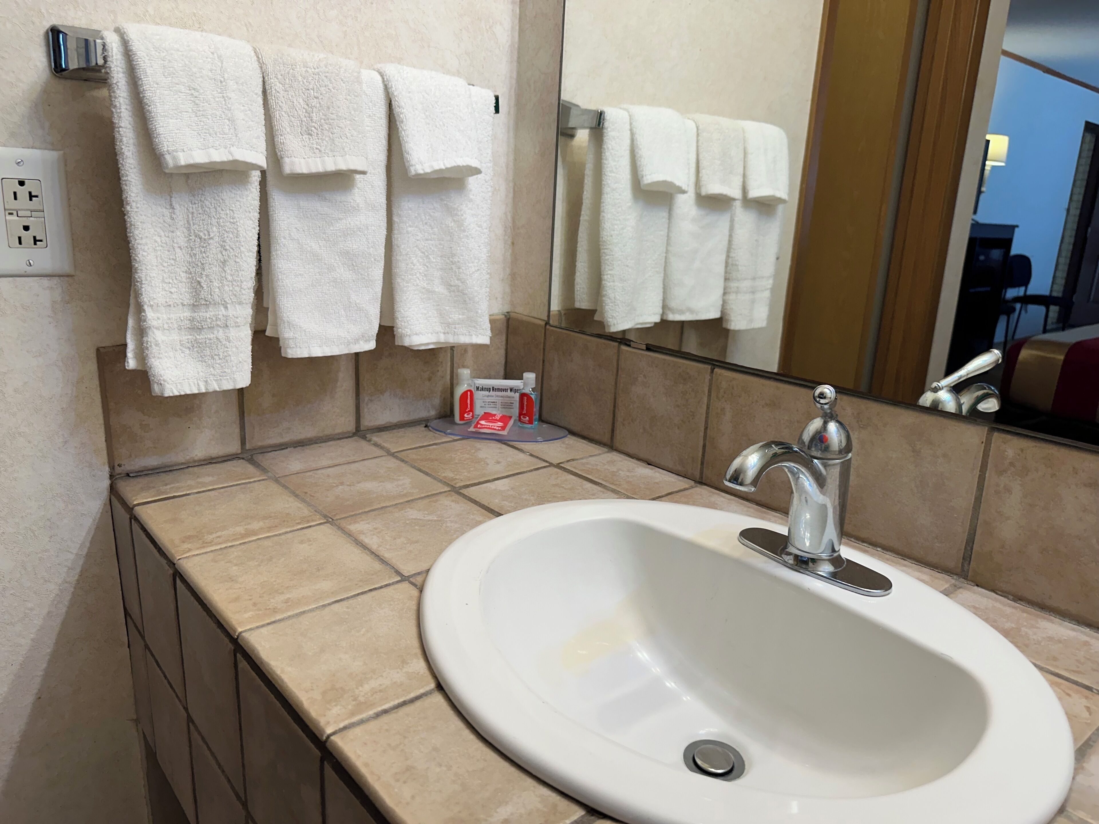 Un baño con lavamanos blanco, espejo y varios toallas blancas colgadas en un perchero.