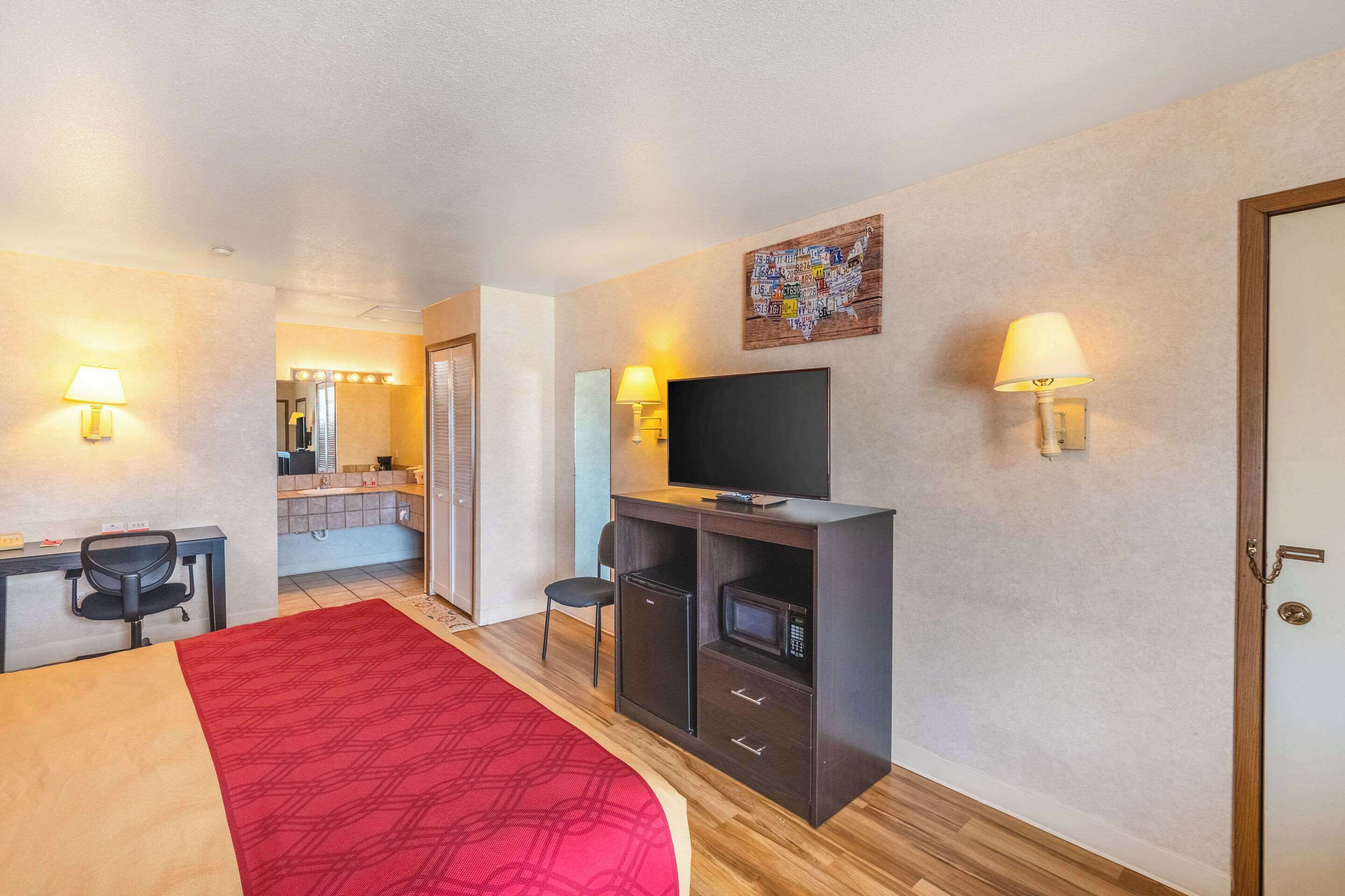 Camera d'albergo con letto, scrivania, sedia, televisore, forno a microonde e piccolo frigorifero.