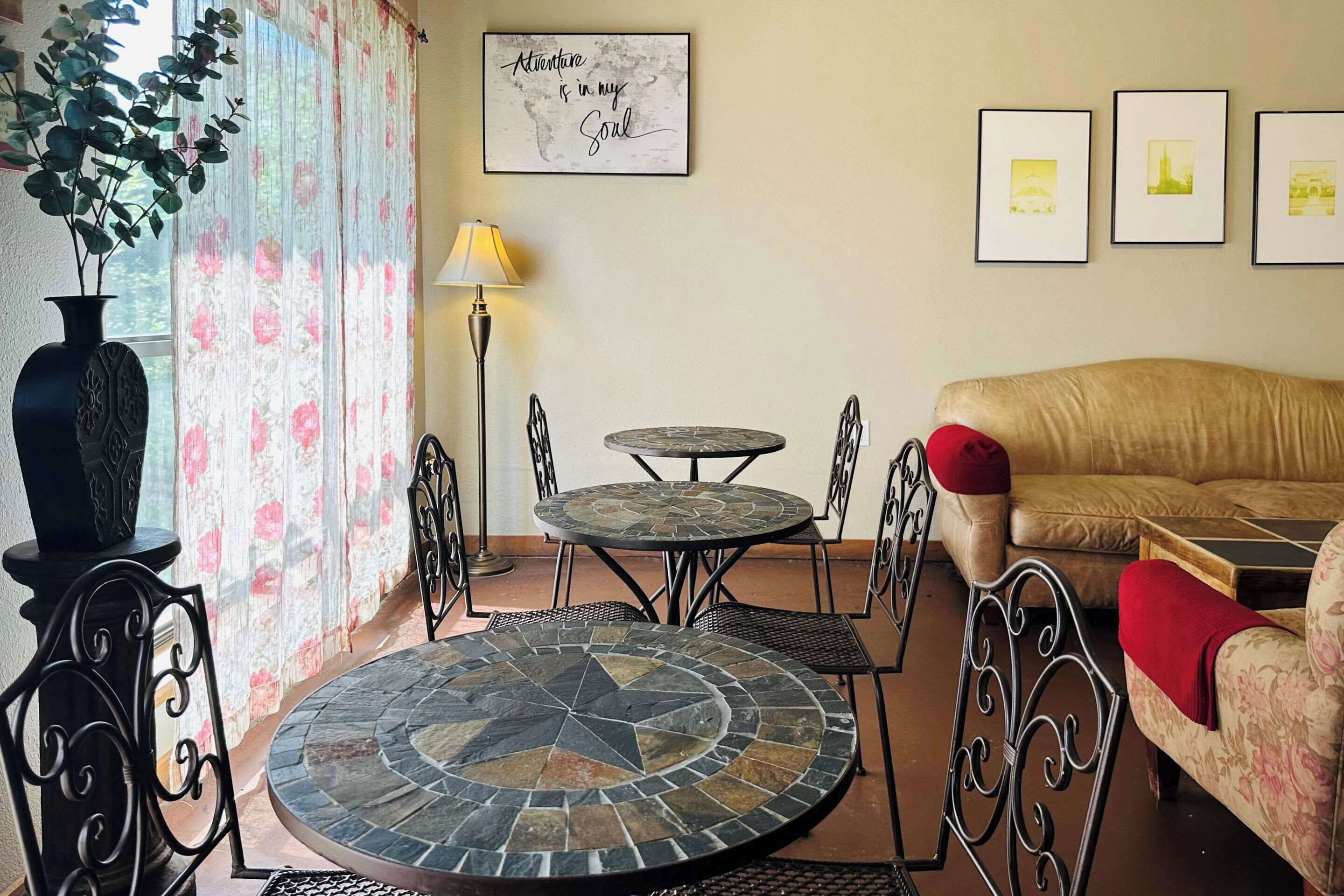 Un salón con una mesa redonda, dos sillones, un sofá, un jarrón decorativo y cuadros enmarcados en la pared.