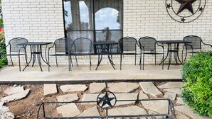 Une terrasse extérieure avec des tables et des chaises en métal noir, un chemin de pierre et l’emblème de l’État du Texas peint sur le mur.