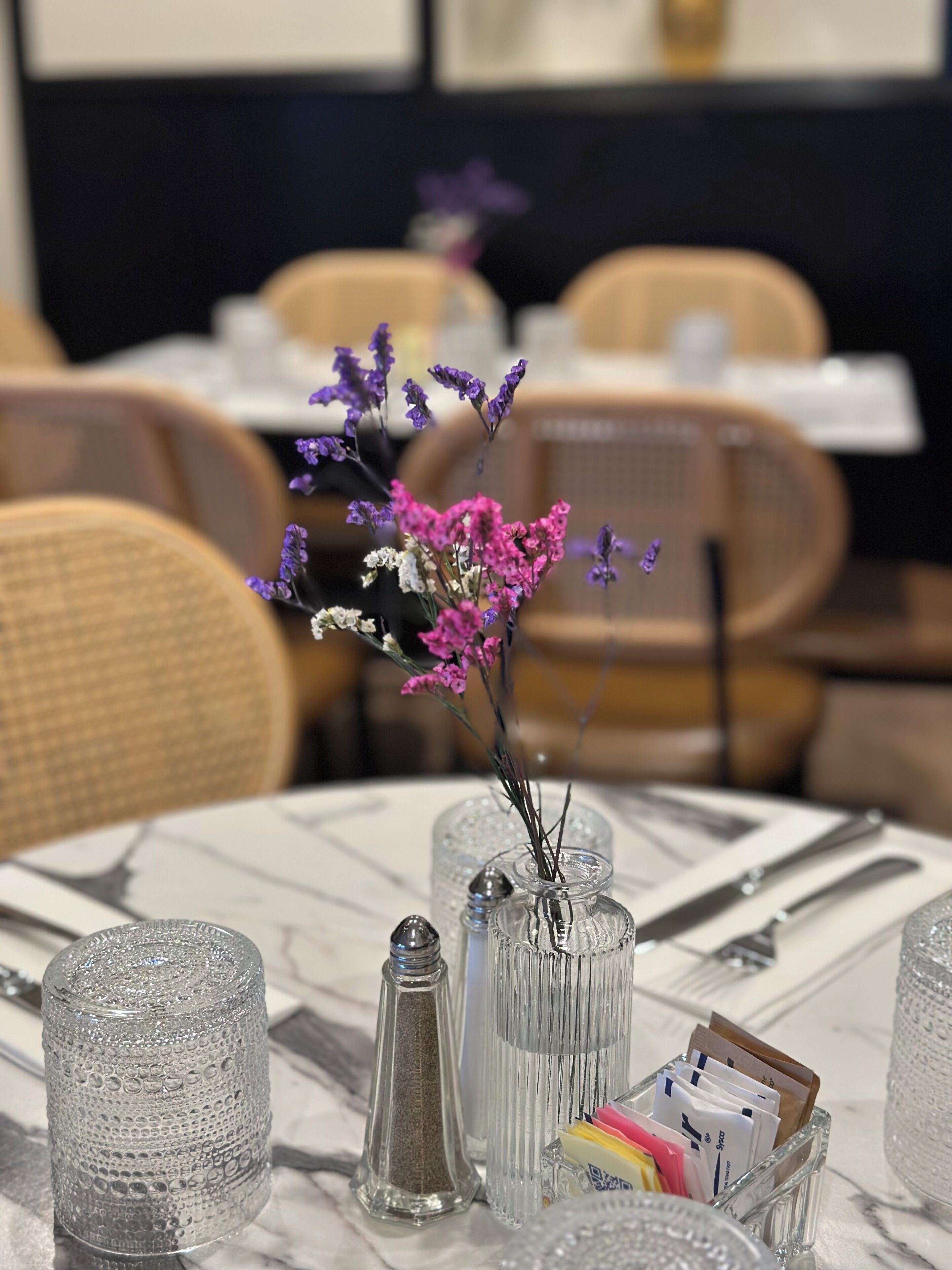 A dining table with a vase of purple flowers, salt and pepper shakers, and a card holder with envelopes.