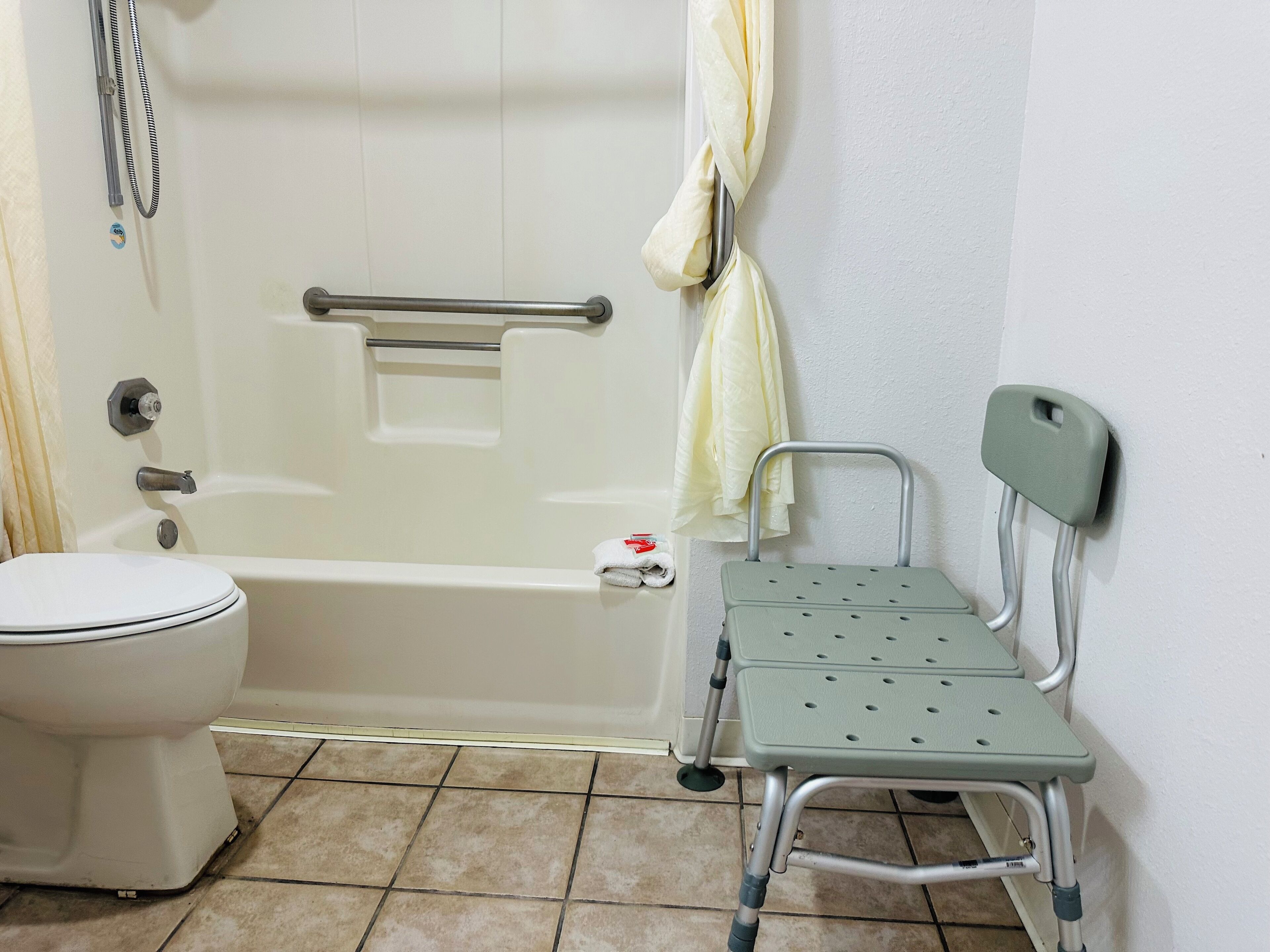 Ein Badezimmer mit Toilette, Badewanne, Dusche und einer rollstuhlgerechten Sitzbank.